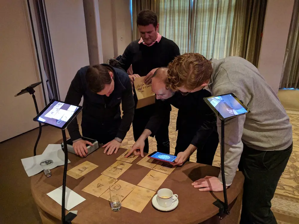 Joueurs penchés sur les iPad et la fiche de jeu de La Machine Infernale
